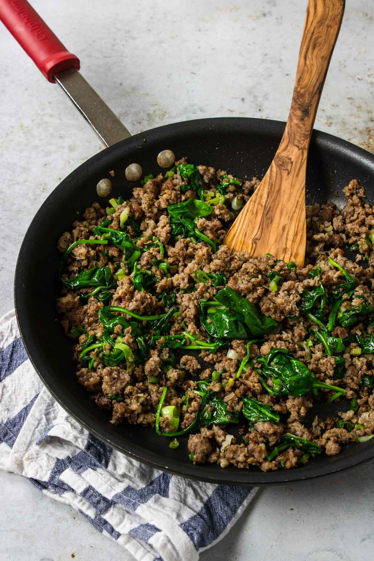 crumbled breakfast sausage with spinach and basil in a skillet