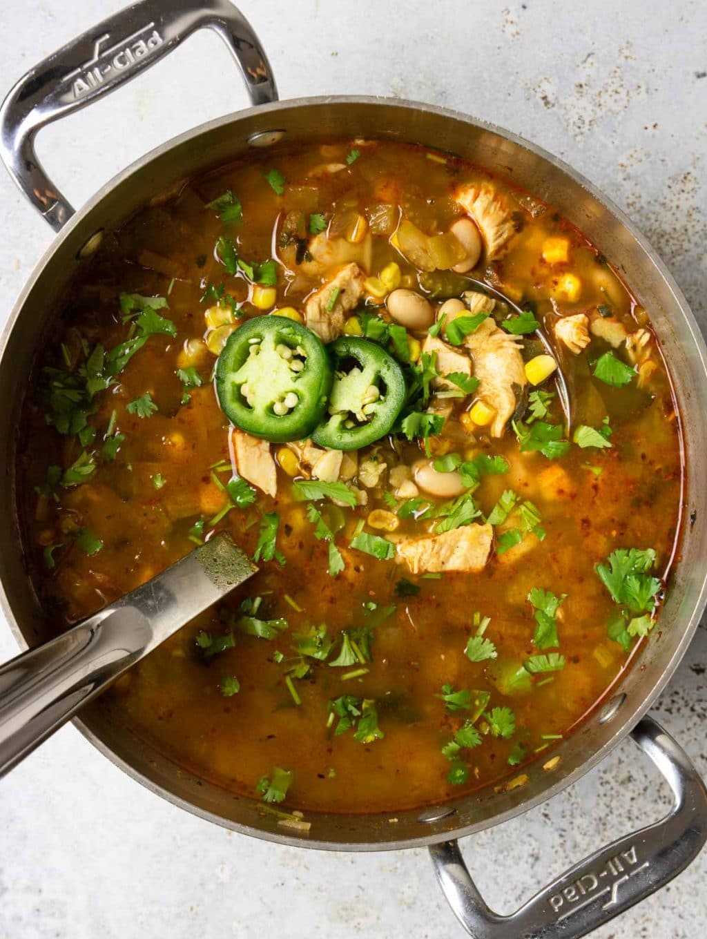 Chicken chili in a large pot with a ladle and garnished with fresh jalapeno and cilantro