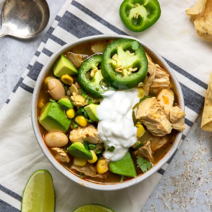 square photo of a bowl of white chicken chili topped with avocado, sour cream, fresh jalapeno and cilantro
