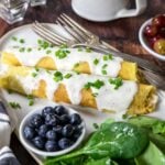 a plate with two chicken crepes topped with béchamel sauce and salad and berries