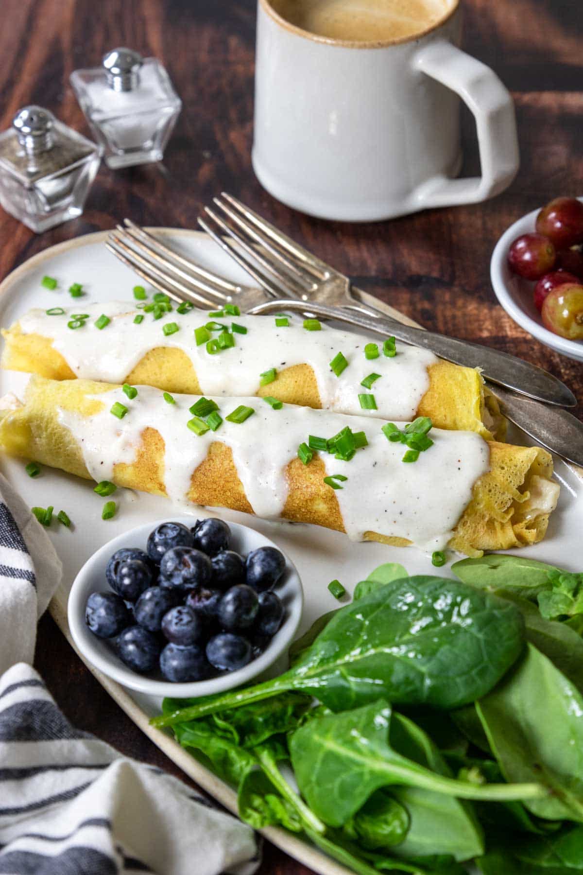 a plate with two chicken crepes topped with béchamel sauce and salad and berries