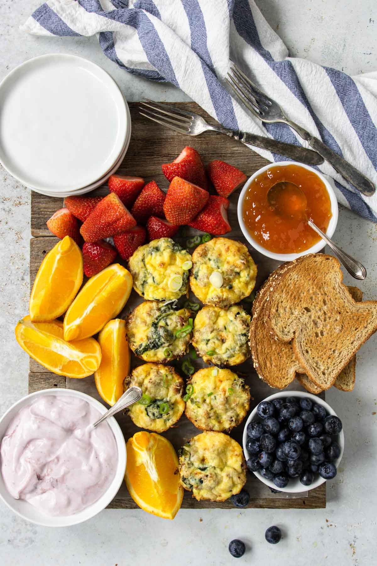 a breakfast board with sausage egg cups, fruit, yogurt and toast