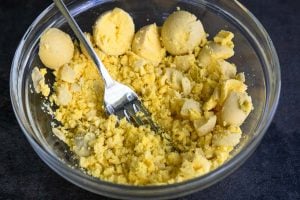 Cooked egg yolks being crumbled with a fork