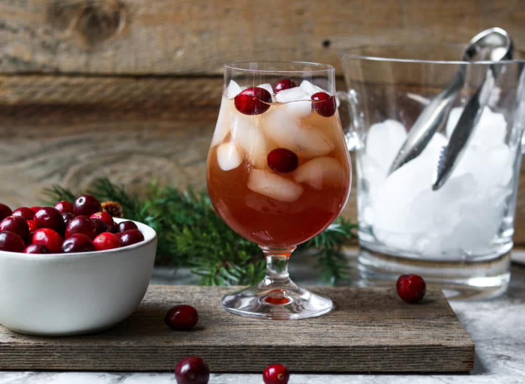 A cranberry white wine spritzer garnished with fresh cranberries, a white bowl of cranberries to the side
