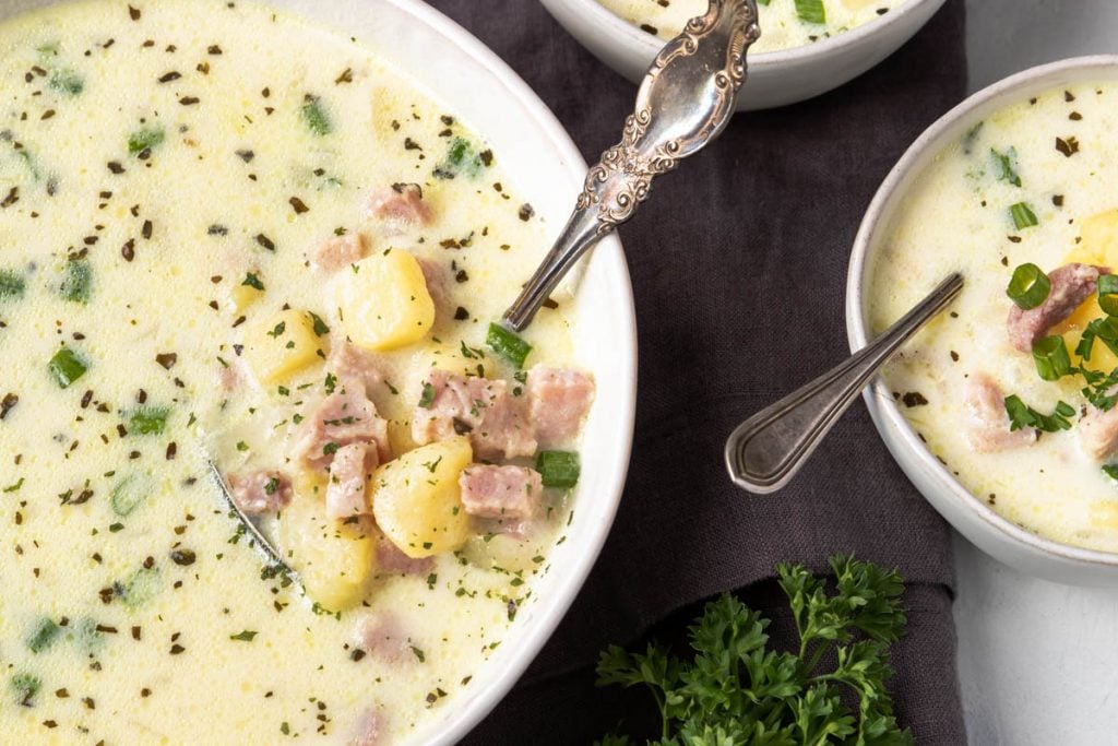 potato and ham chowder being served out of a large bowl into smaller white bowls, garnished with green onions and parsley