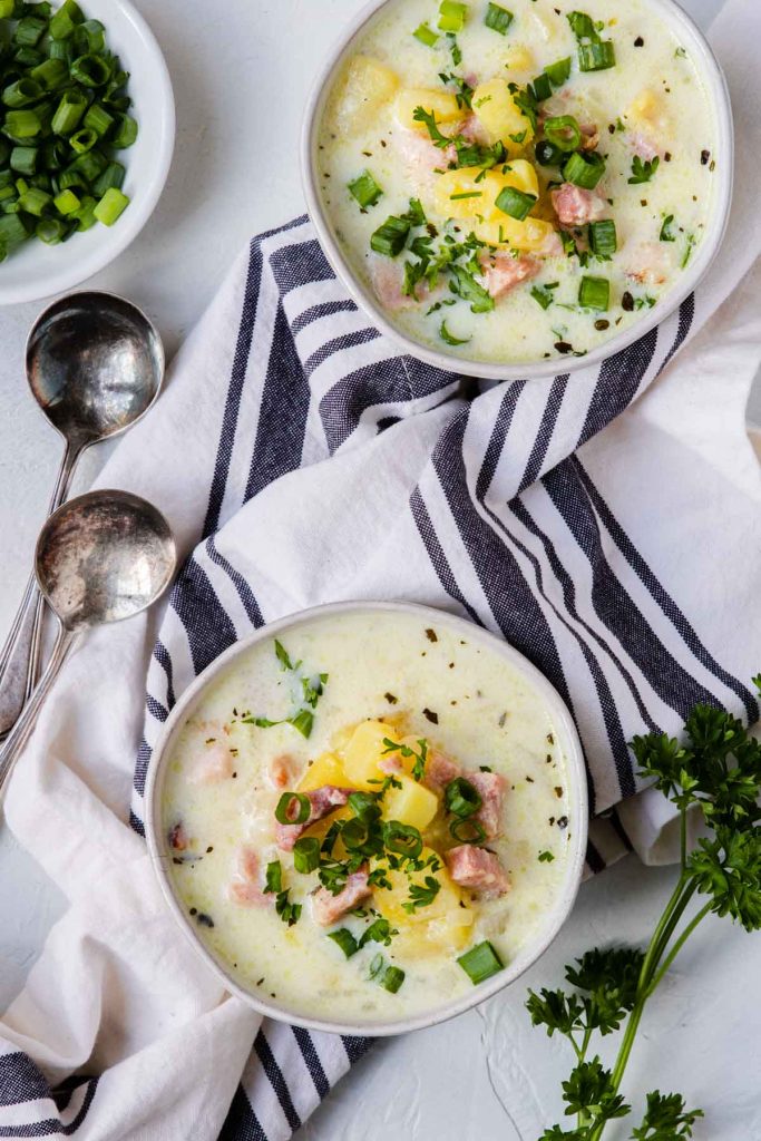 Ham and Potato Chowder in two white bowls over a napkin with green onions and parsley on top