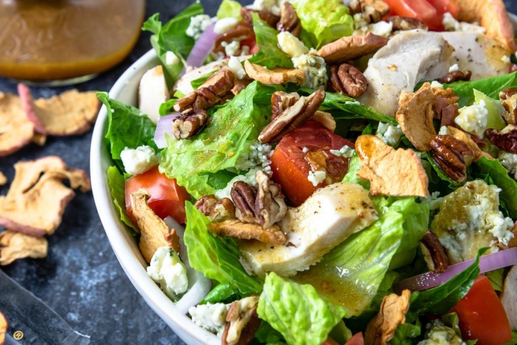 Apple Pecan Chicken Salad in a white bowl with dressing and apple chips to the side