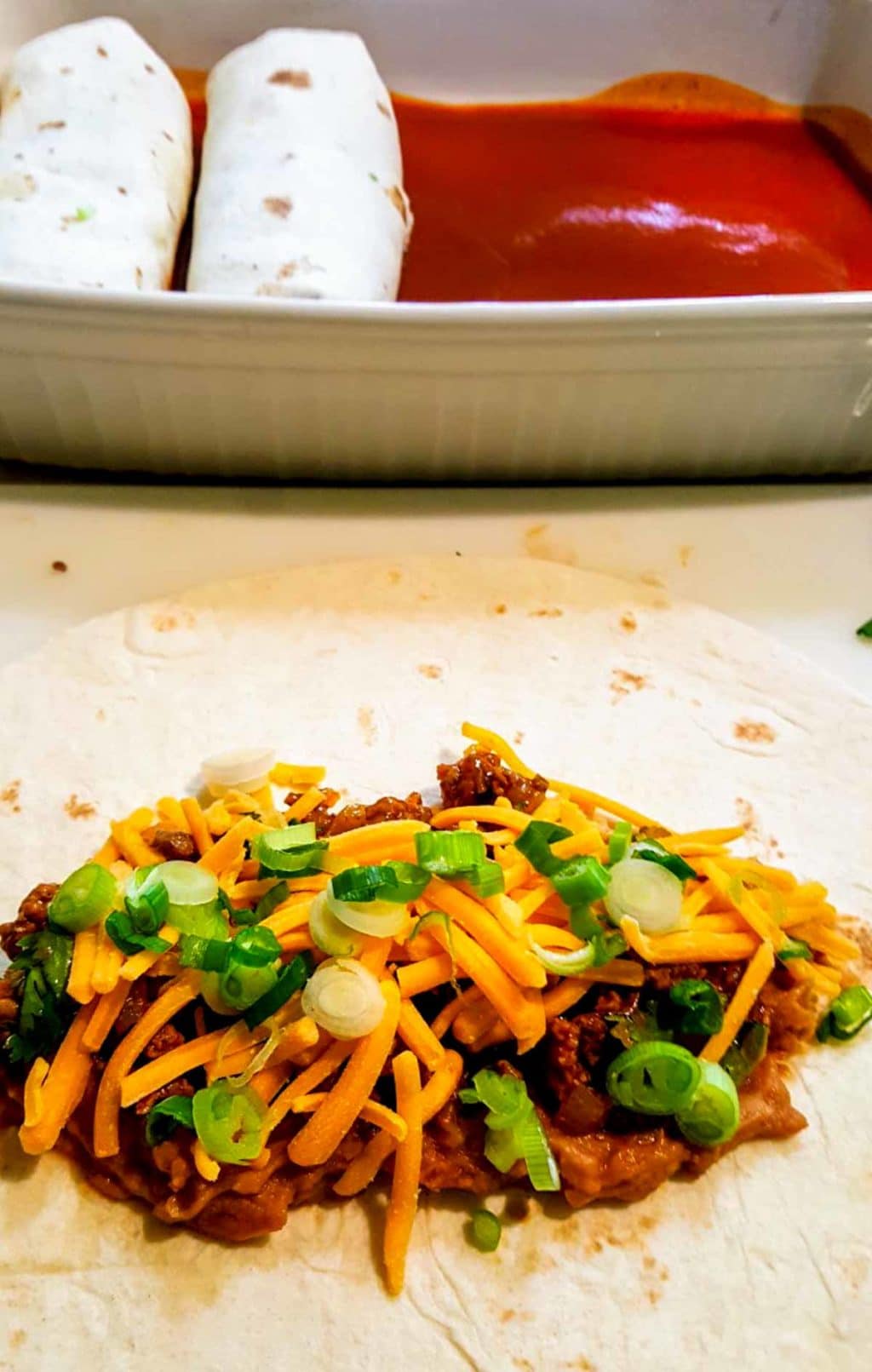 The filling of an Enchirito on a flour tortilla, a pan of rolled Enchiritos in the background