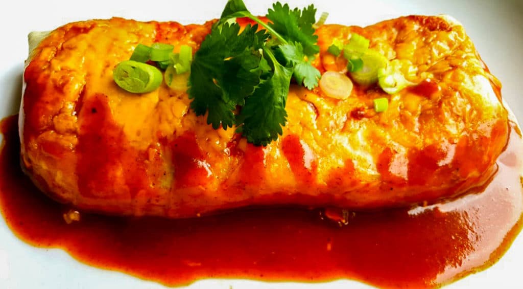 1 Enchirito on a white plate smothered in red sauce and cheese, garnished with green onions and cilantro