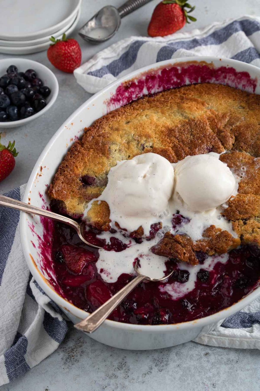 mixed berry cobbler with two spoons and two scoops of vanilla ice cream