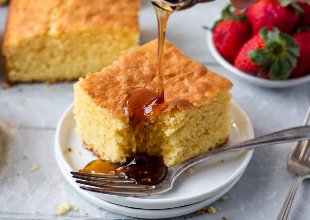 a piece of best ever cornbread on a white plate being drizzled with syrup