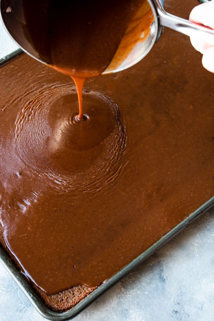 boiled chocolate frosting being poured onto the chocolate sheet cake