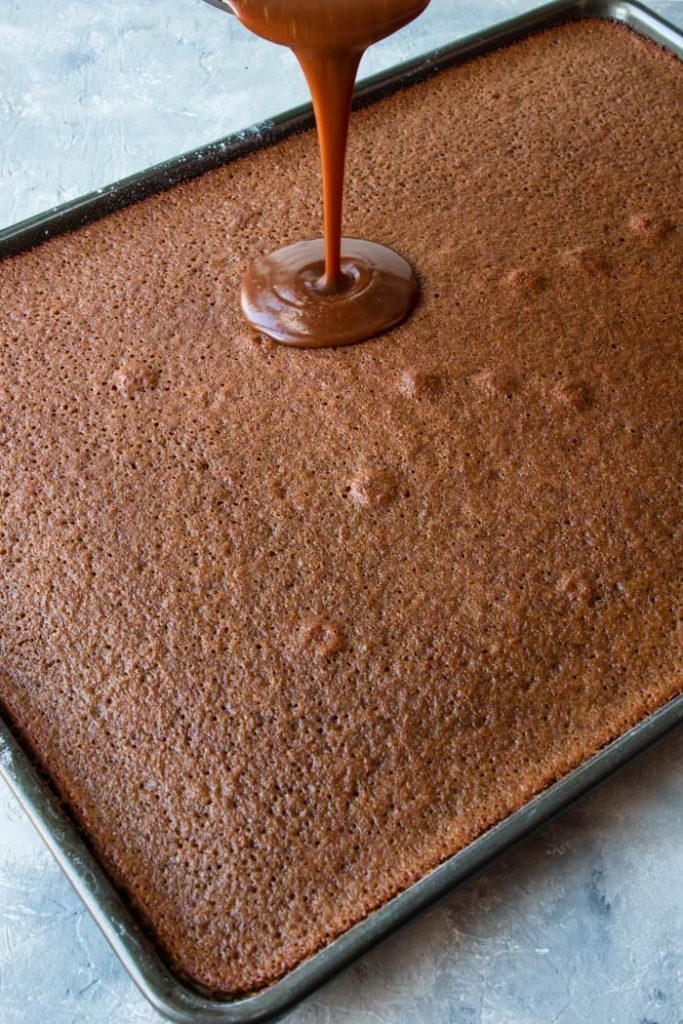 step 1 frosting being poured onto chocolate cake