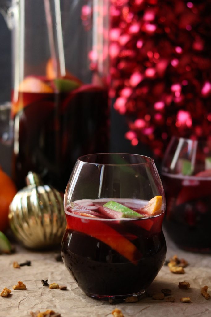 A glass of winter sangria mixed with fruit, holiday decorations in the background