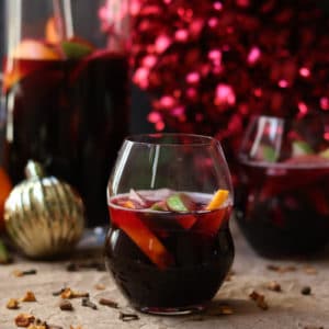 a glass of winter sangria red wine surrounded by citrus fruit and christmas ornaments