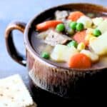 A bowl of steak soup with crackers to the side