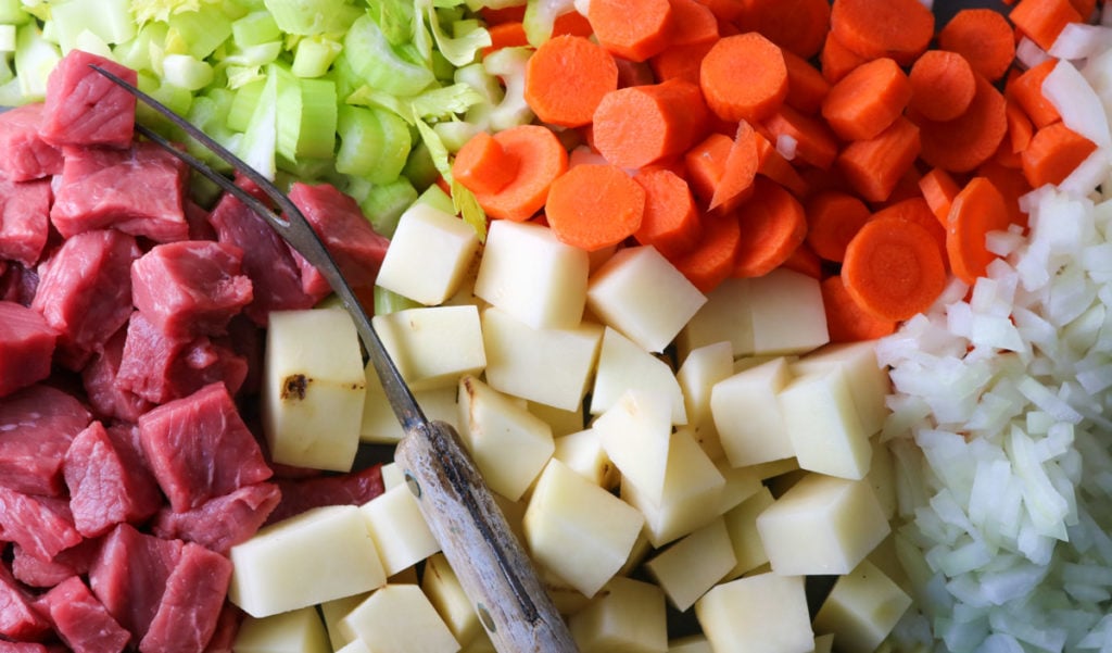 A close up picture of a lot of the ingredients that go into the steak soup: beef, potatoes, onions, carrots, and celery