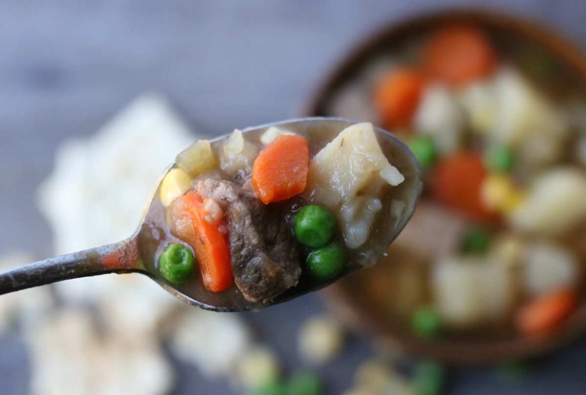 A spoon full of Instant Pot Steak Soup with beef, carrots, corn, potatoes, and peas