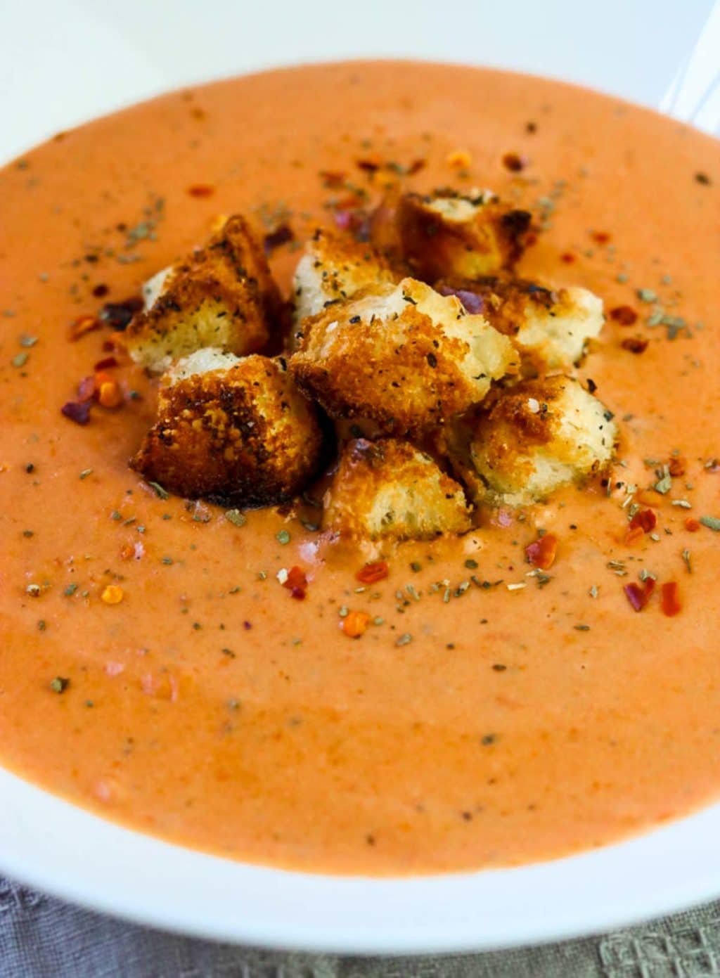 a white bowl full of tomato basil soup topped with garlic croutons