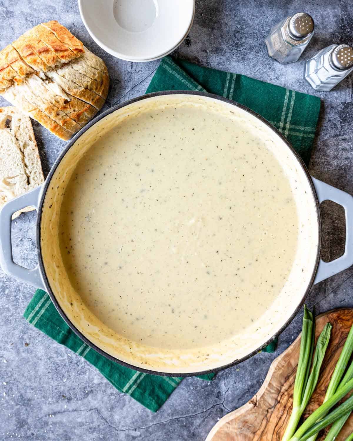 a large pot of cauliflower potato soup with bread and green onions to the side