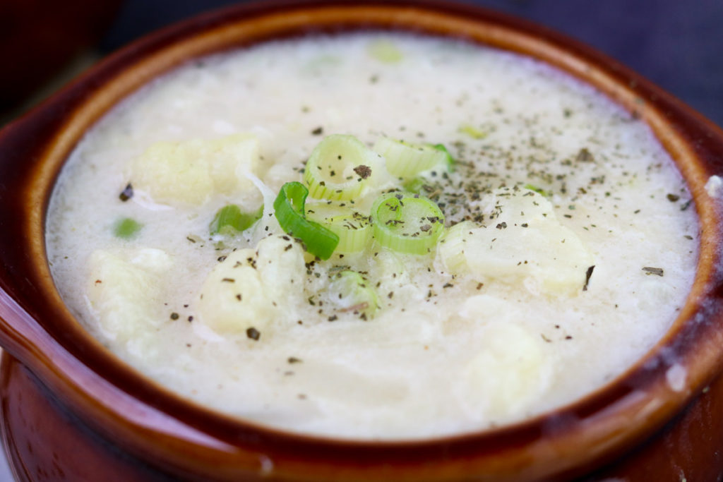 Cauliflower and Potato Chowder in a brown bowl with green onions and dried basil on top