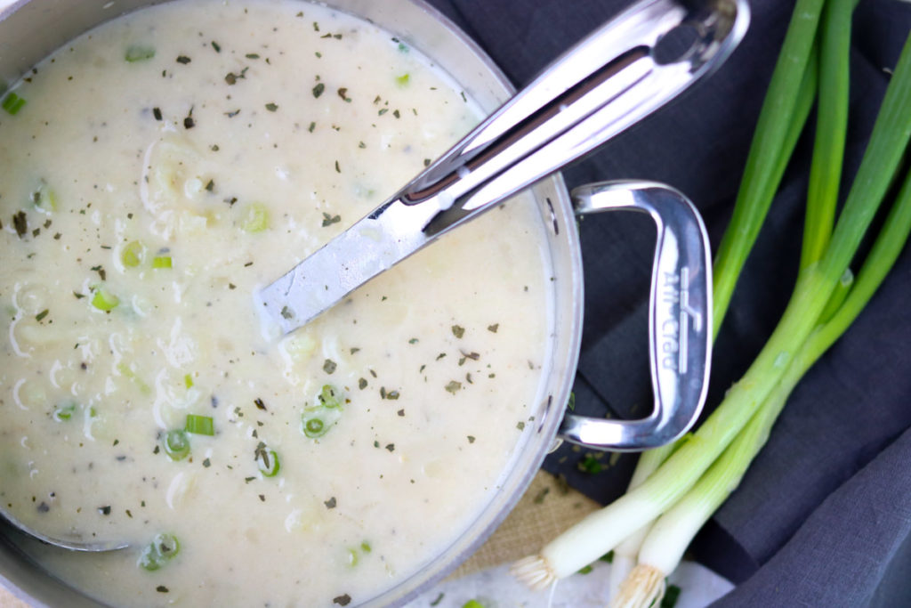 Cauliflower and Potato Chowder in an All-Clad pot with a ladle and green onions to the side momsdinner.net