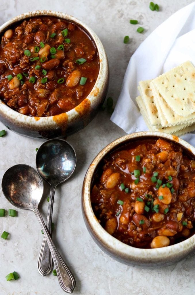 classic chili in two crocks with green onions on top and two spoons to the side