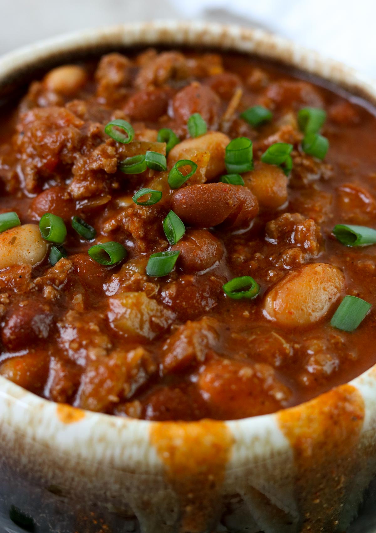 Up close picture of thick chili with beans and tomatoes topped with green onions