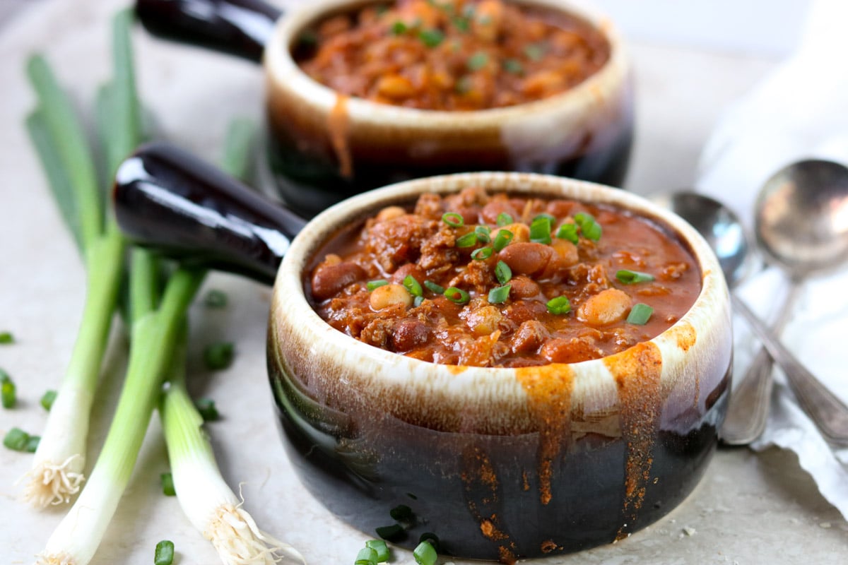 two bowls of classic chili and green onions to the side