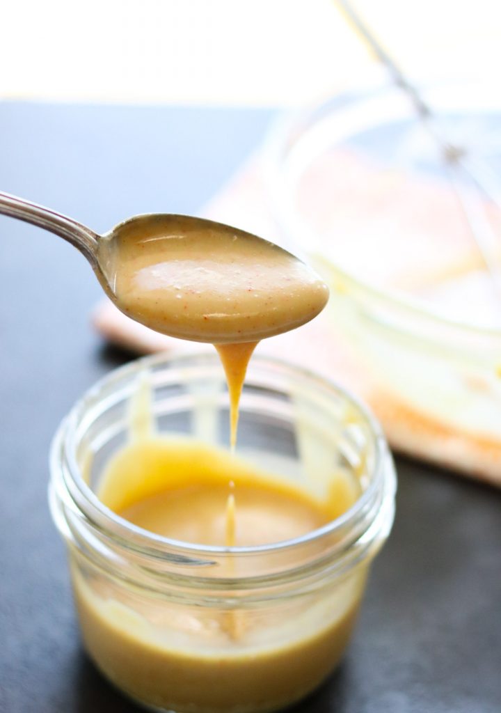 honey mustard sauce being dripped from a spoon into a mason jar.
