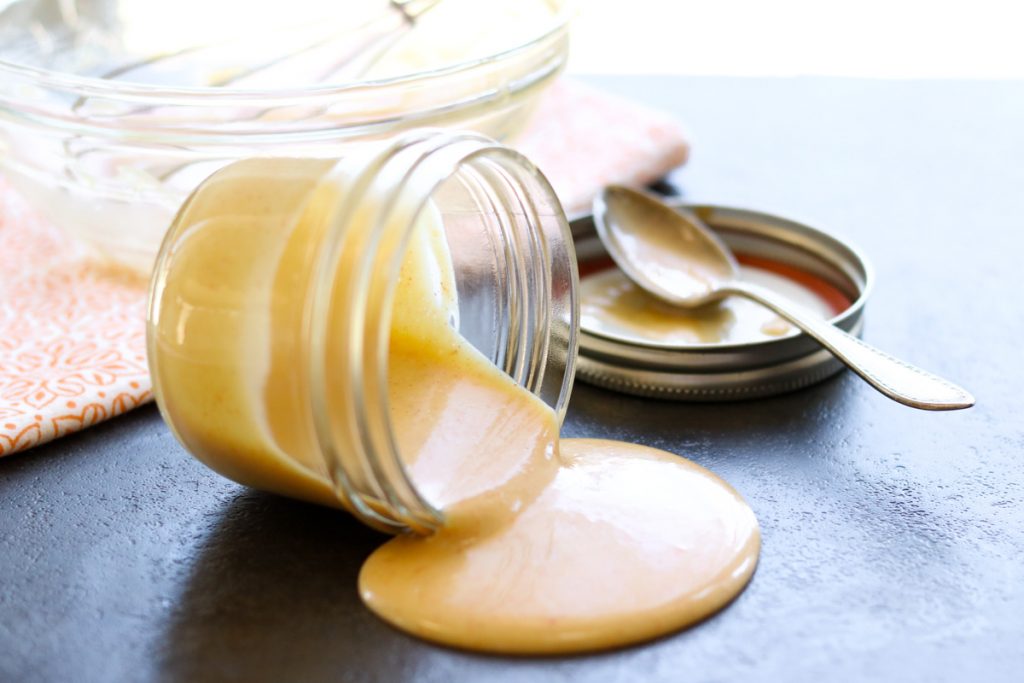 Honey Mustard Sauce in a mason jar spilled over on the counter, with a spoon and the mason jar lid in the background