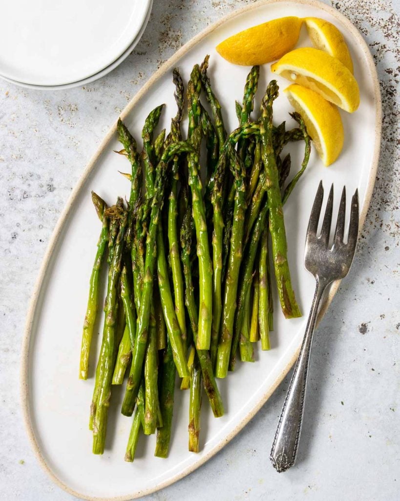 Oven Roasted Asparagus on a white plate with lemon wedges