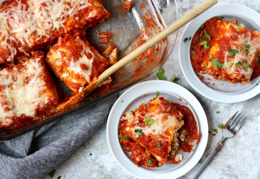 two plates with 1 lasagna roll up each and the baking pan full of lasagna roll ups to the side www.momsdinner.net