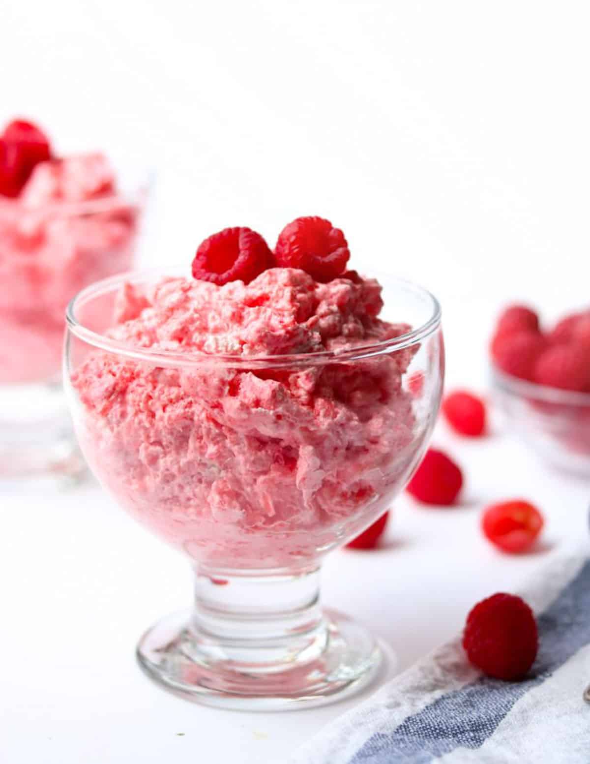 Raspberry Jello Salad in a glass topped with raspberries