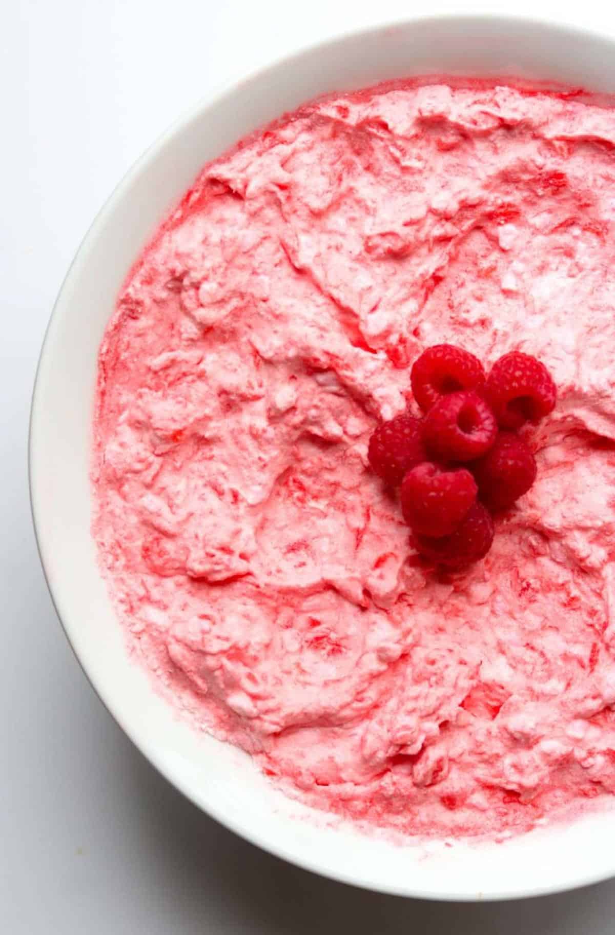 Large white bowl of raspberry jello salad with raspberries on top