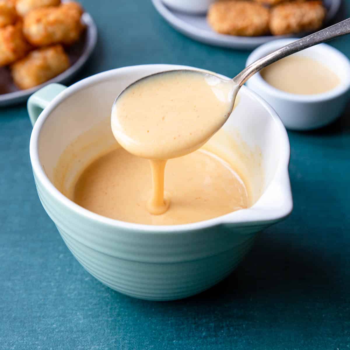a spoon pouring honey mustard into a measuring cup