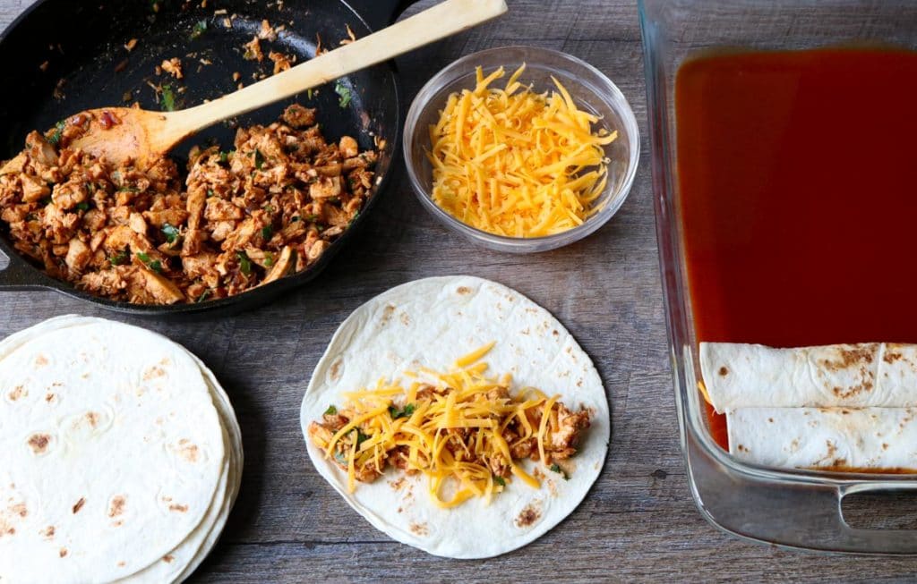  Chicken Enchilada assembly line: flour tortillas, chicken enchilada filling, cheese, baking pan with enchilada sauce momsdinner.net