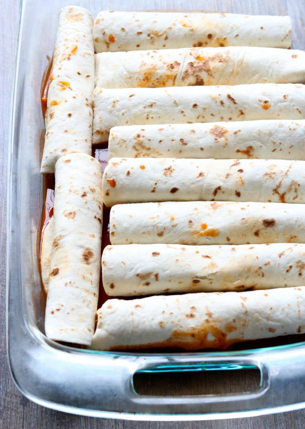 Flour tortillas rolled with chicken enchilada filling in a glass baking dish momsdinner.net