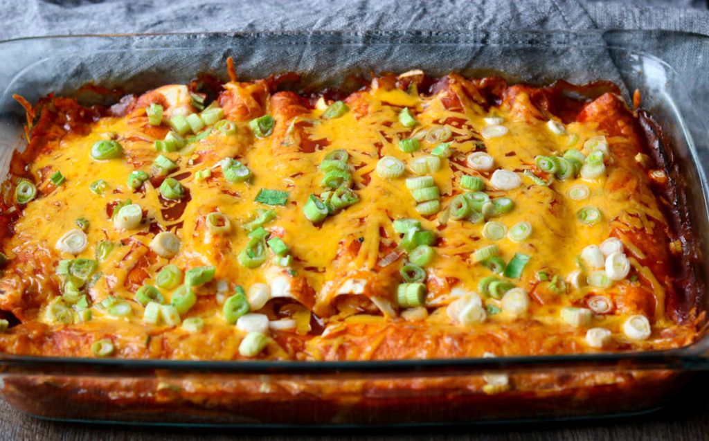 Chicken Enchiladas in a glass casserole pan garnished with green onions momsdinner.net