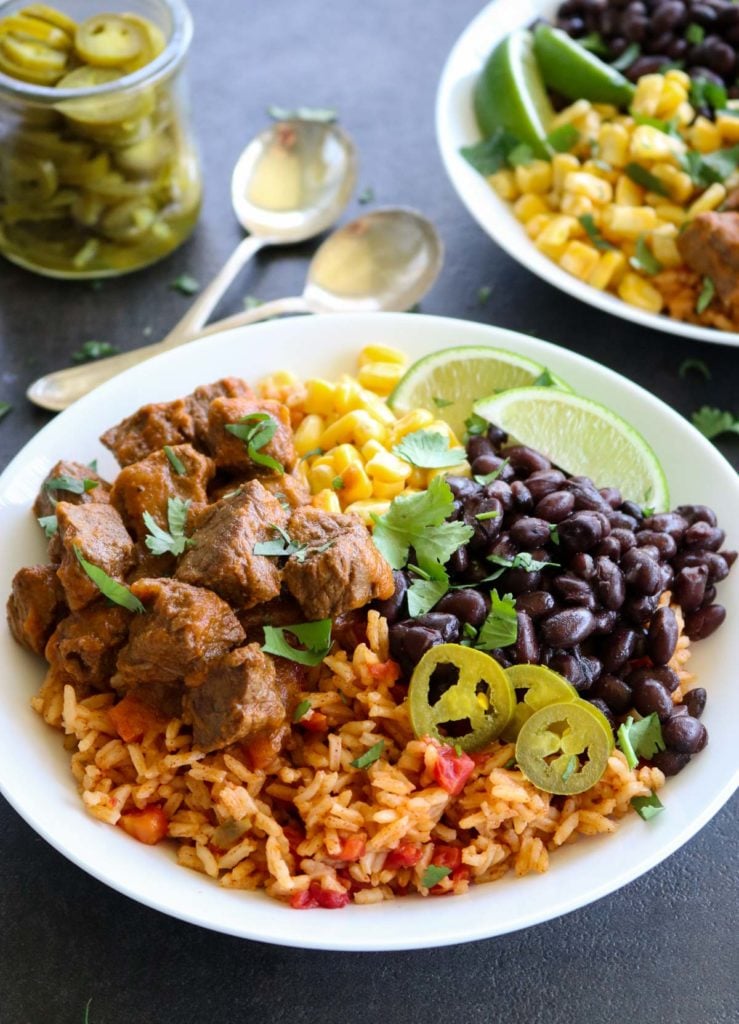 rice, steak, black beans, corn, and limes in a white bowl.