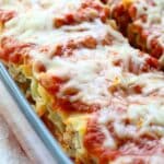 a glass baking dish full of sausage lasagna roll ups topped with sauce and melted cheese.