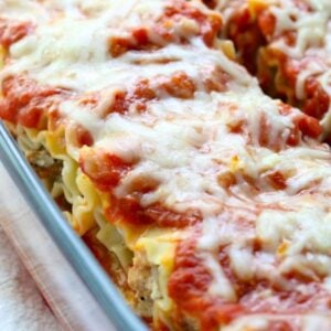 a glass baking dish full of sausage lasagna roll ups topped with sauce and melted cheese.