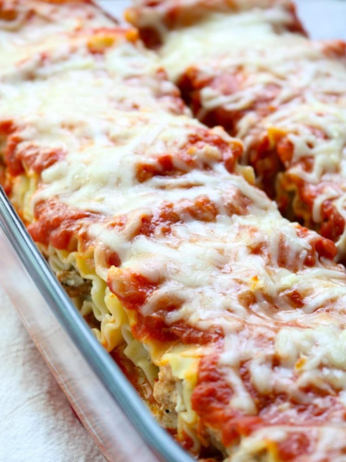 A pan full of lasagna roll ups topped with sauce and melted cheese. 