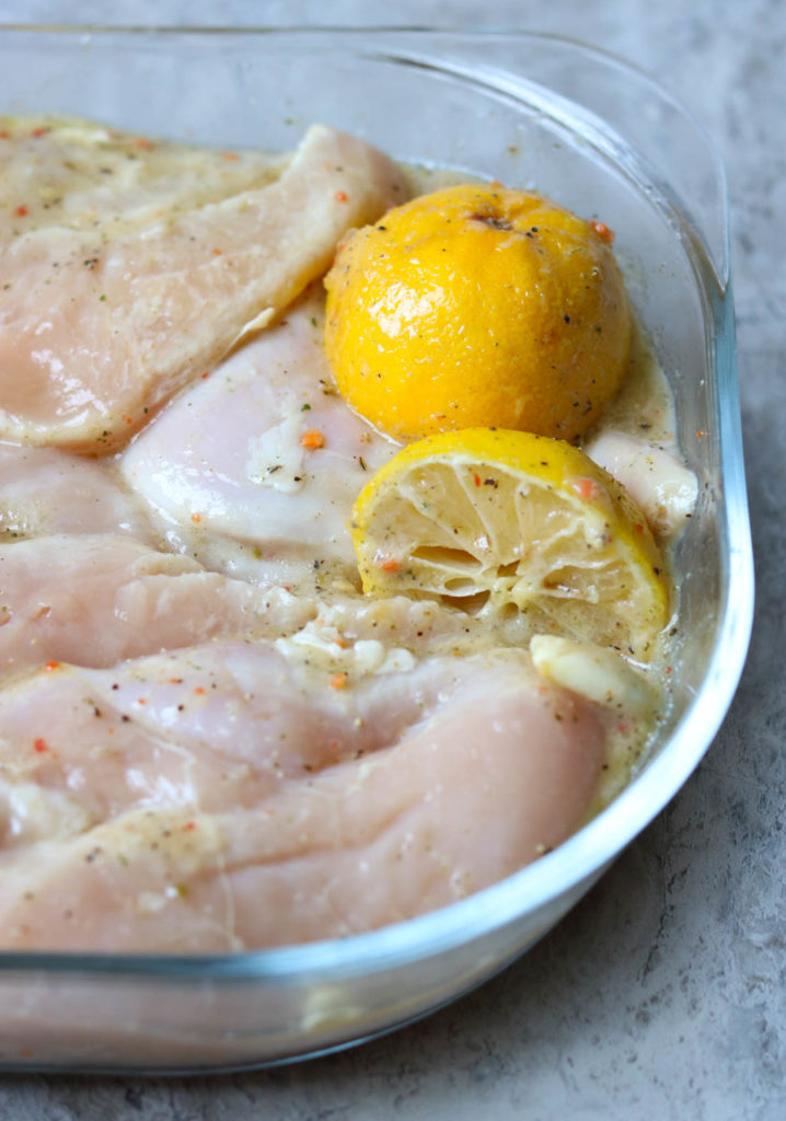 raw chicken marinating in a glass dish with two lemons momsdinner.net