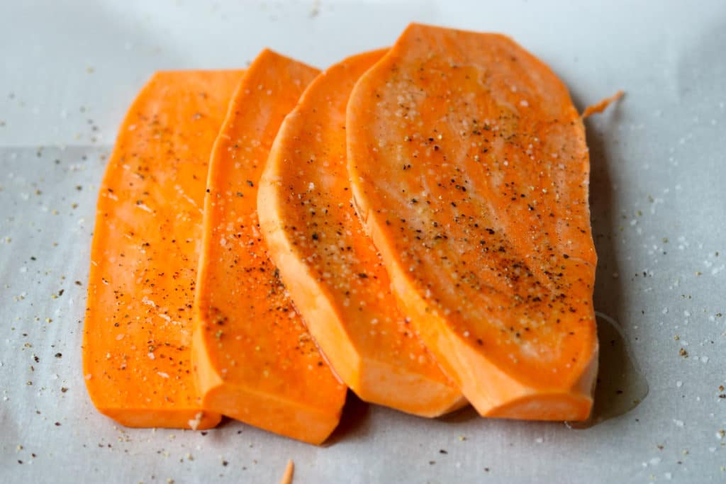 Fresh cut sweet potatoes on parchment with salt and pepper