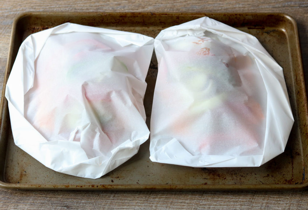 two chicken parchment packets folded on a sheet pan