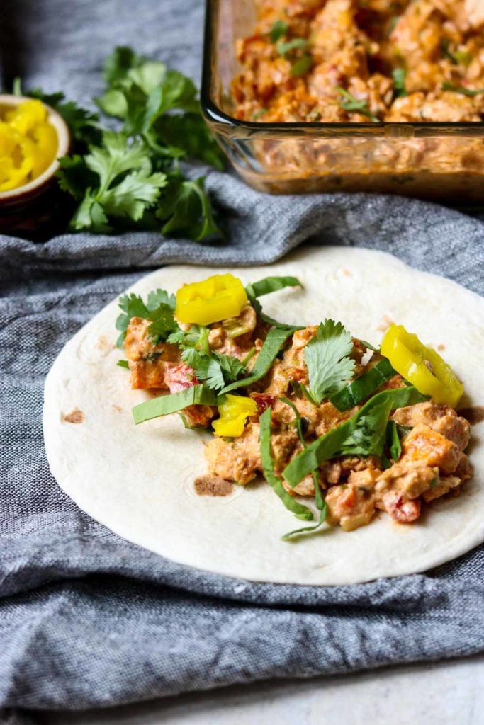 Creamy Chicken Taco on a flour tortilla, glass baking dish full of chicken taco meat in the background