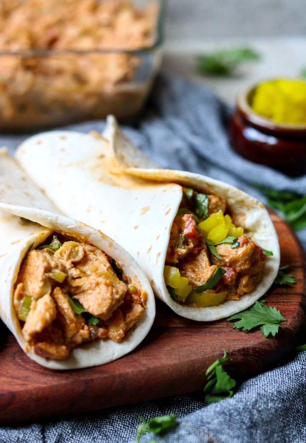 Two soft shell tacos with chicken filling, sitting on a wooden cutting board