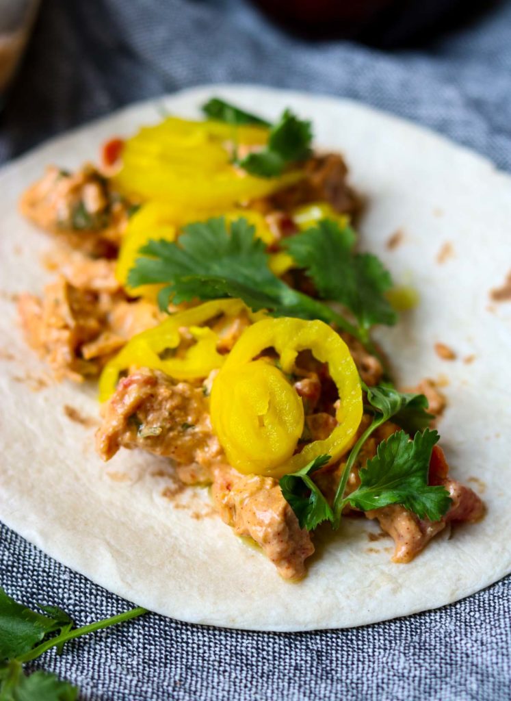 A flour tortilla laid out with creamy chicken taco filling, pepperoncinis and cilantro