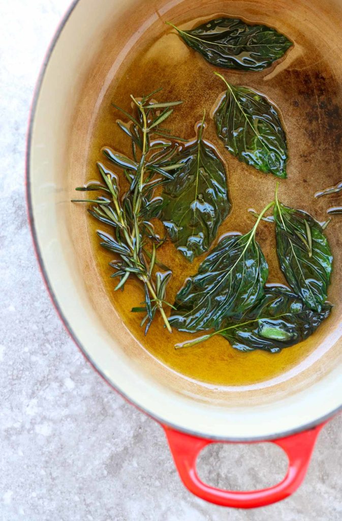 basil and rosemary in oil in a dutch oven pot